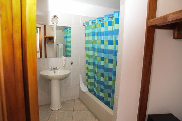 Baño completo con bañera y cortina de ducha azul en Negril Treehouse Resort Jamaica