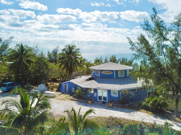 Vista aérea del The Sunset Cove and Rainbow Inn, edificio azul rodeado de palmeras con vistas al mar Caribe