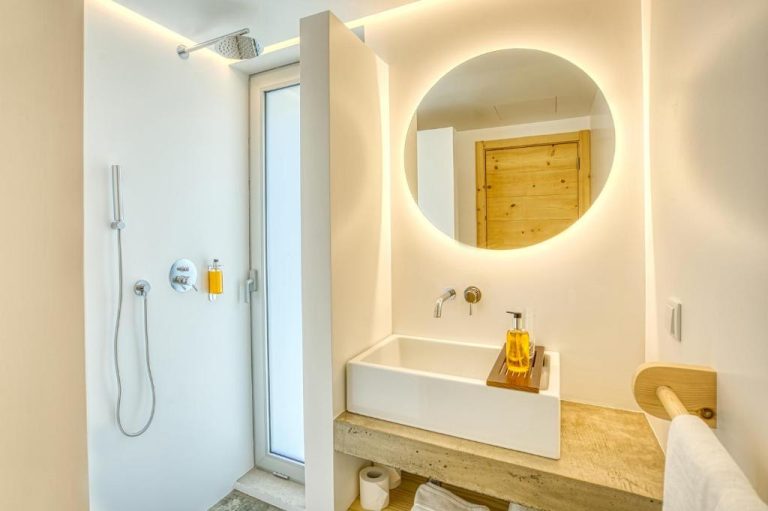 Baño moderno con ducha, lavabo empotrado y espejo redondo iluminado en Socalco Nature Calheta