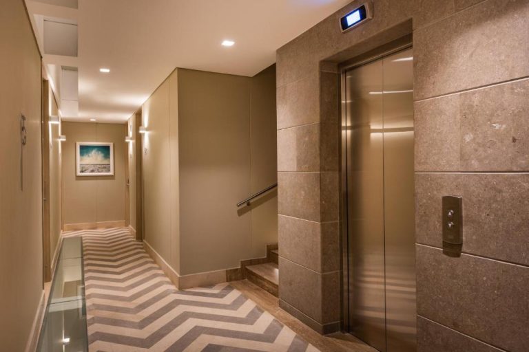 Pasillo y ascensor de lujo con revestimiento de piedra y suelo de chevron en Oz Hotel Luxury