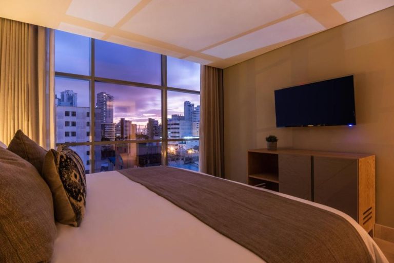 Habitación de lujo con cama doble y vista panorámica de la ciudad al atardecer en Oz Hotel Luxury