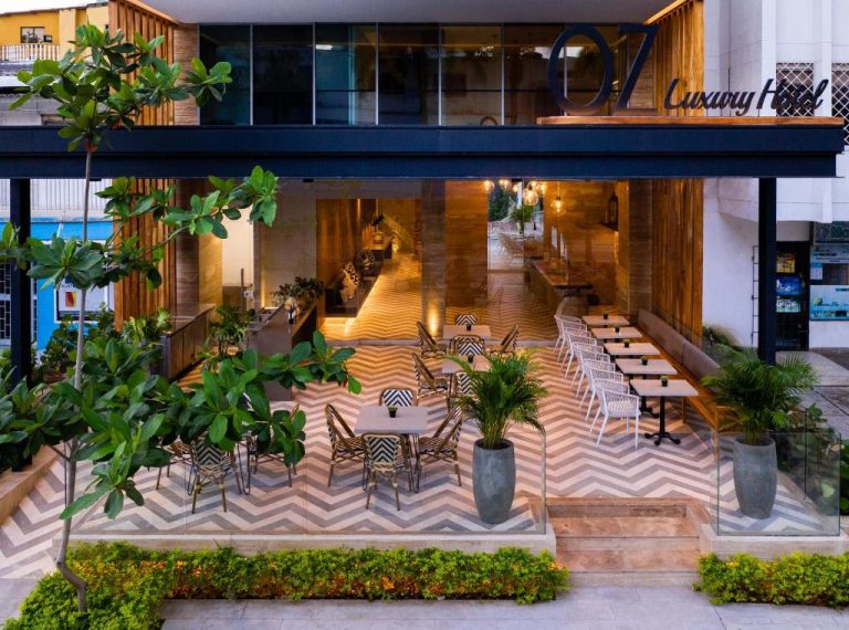 Terraza exterior con mesas y sillas del Oz Hotel Luxury, decorada con plantas tropicales y suelo en zigzag
