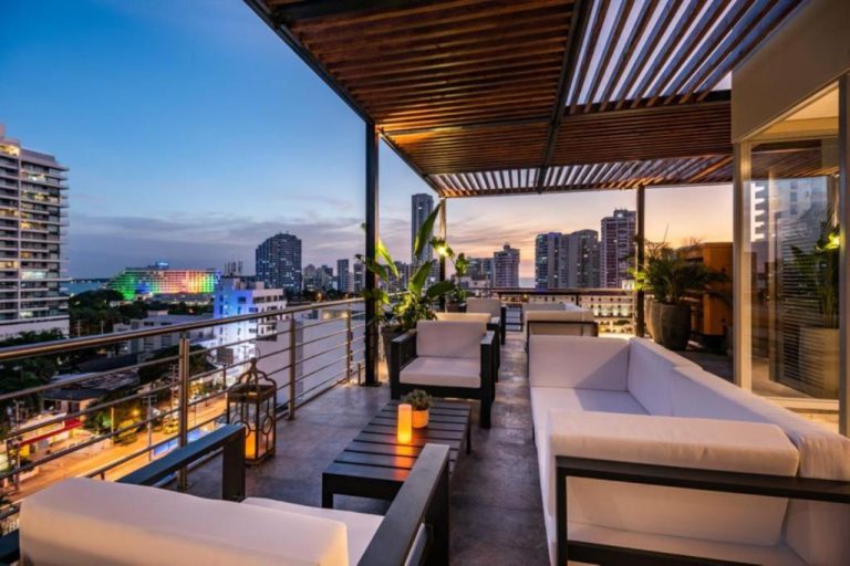 Terraza lounge con sofás blancos y vistas panorámicas nocturnas de la ciudad en Oz Hotel Luxury
