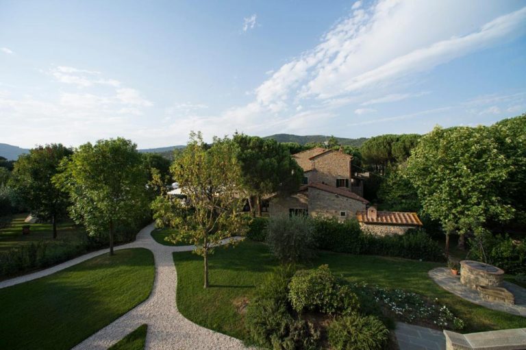 Jardín exterior con senderos y edificio de piedra toscano del Relais La Corte dei Papi