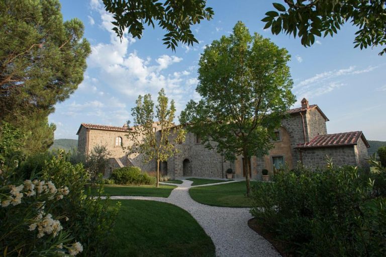 Fachada exterior de piedra del Relais La Corte dei Papi rodeada de jardines y árboles en la Toscana
