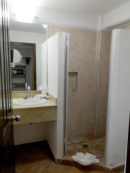 Baño con ducha de azulejos y lavabo en mármol del Hotel El Pescador con espejo y toallas