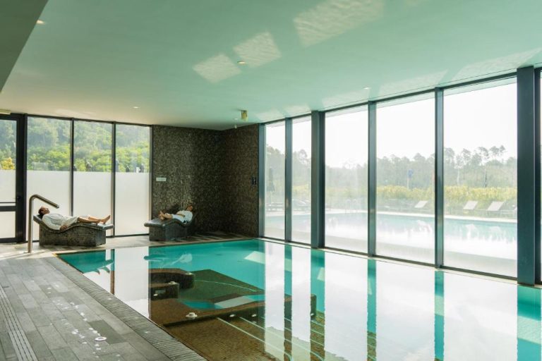 Piscina interior climatizada con tumbonas y vistas al bosque en Monchique Resort & Spa