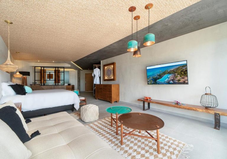 Suite amplia con zona de estar, cama doble y TV en pared del Mvngata Beach Hotel