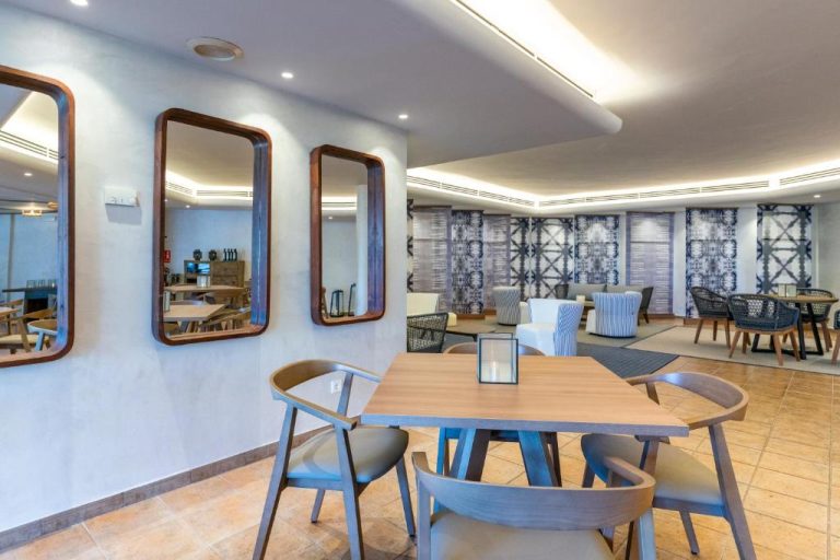 Salón comedor con mesas de madera, espejos decorativos y zona lounge del Calallonga Hotel Menorca