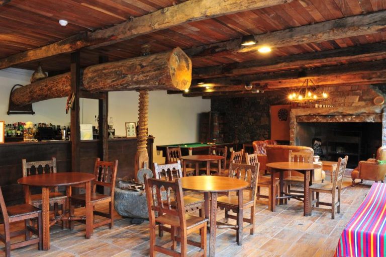 Bar rústico con chimenea de piedra, vigas de madera y mesas de madera en Estalagem do Vale