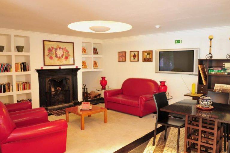 Salón con chimenea y sofás rojos de cuero en Estalagem do Vale, con televisión y estanterías