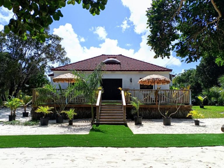 Fachada exterior de The Pilot House con terraza de madera, sombrillas tropicales y jardín frente a la playa