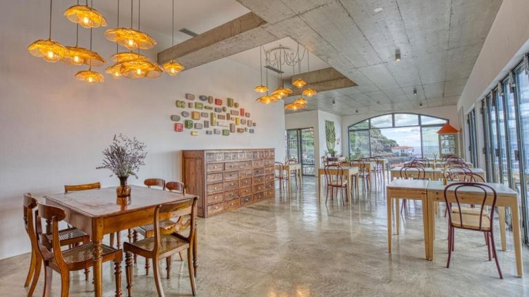 Restaurante interior del Socalco Nature Calheta con mesas de madera, lámparas artesanales y vistas al mar