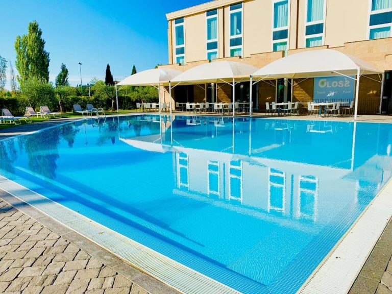Piscina exterior con sombrillas y zona de restaurante del A Point Arezzo Park Hotel en Italia