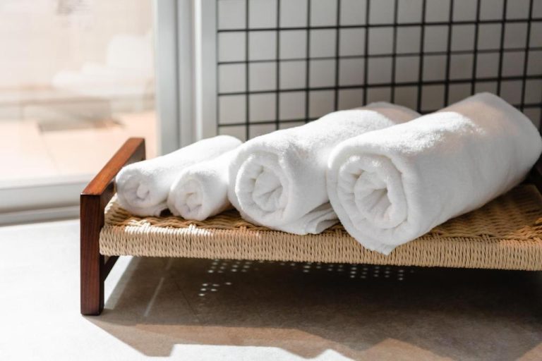 Toallas blancas enrolladas sobre bandeja de mimbre en el baño del Prostyle Ryokan Naha Kenchou Mae