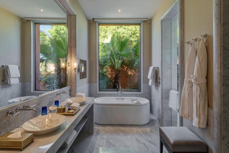 Lujoso baño de mármol con bañera exenta y vistas al jardín en The Oberoi Marrakech