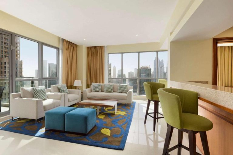 Amplia sala de estar con sofás blancos y vistas al skyline en Ramada by Wyndham Downtown Dubai