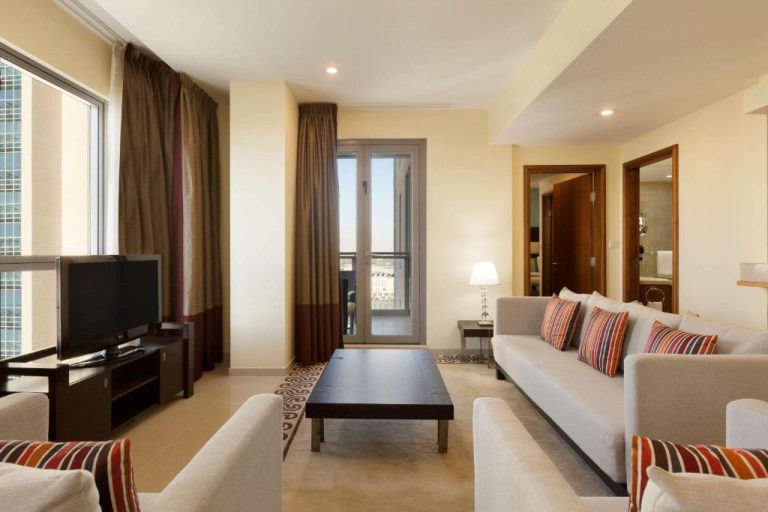 Amplio salón de suite con sofás, mesa de centro y balcón en Ramada by Wyndham Downtown Dubai