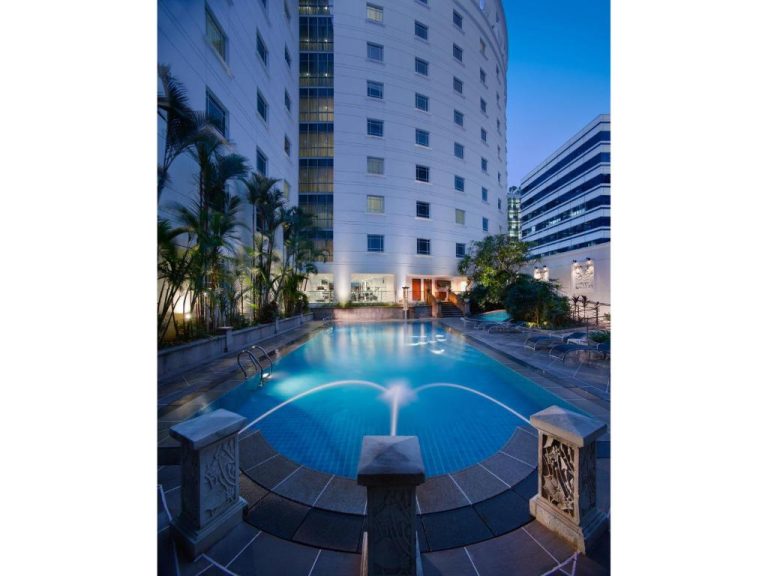 Piscina exterior iluminada con fuente del Rendezvous Hotel Singapore by Far East Hospitality al atardecer