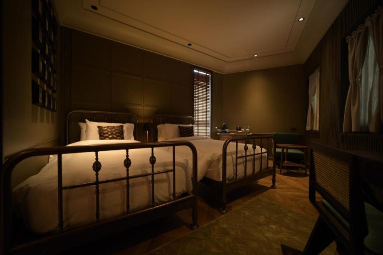 Habitación twin con camas de hierro forjado estilo vintage y decoración oscura en Hotel Verdigris