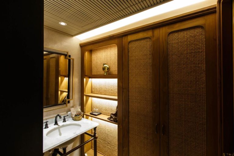 Baño elegante con armario de ratán y estantes iluminados en el Hotel Verdigris