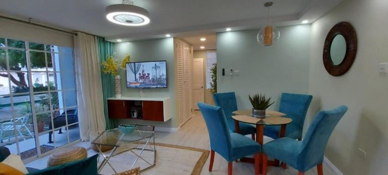 Sala comedor moderna con sillas azules y TV en apartamento del Almond Grove at Sand Castle