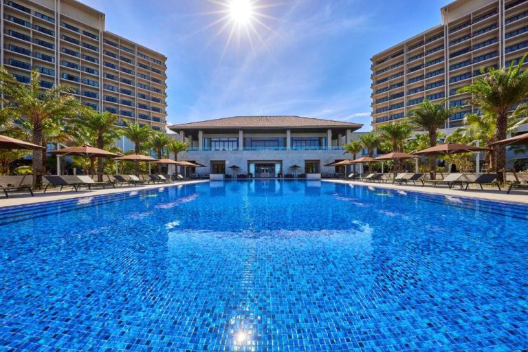 Gran piscina exterior con tumbonas y palmeras del Ryukyu Hotel & Resort Nashiro Beach en Okinawa