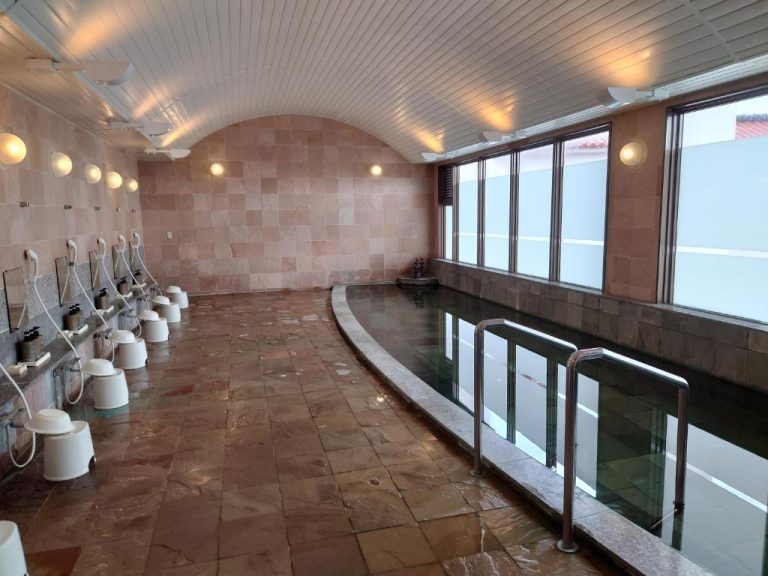 Baño termal onsen interior con piscina y duchas individuales en Ishigaki Seaside Hotel, Japón