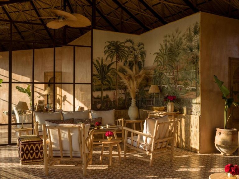 Salón con muebles de madera natural y mural tropical en Casa Abracadabra, ambiente boho con techo de paja