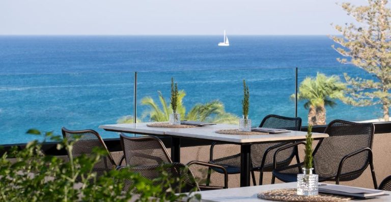 Terraza del restaurante del Ella Helea con mesas y vistas al mar azul y velero al fondo