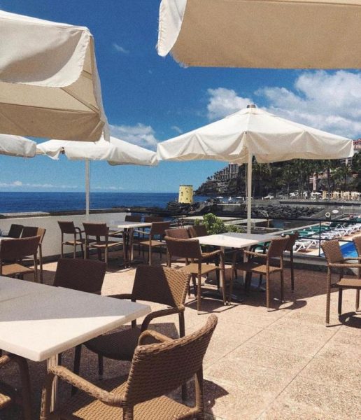 Terraza exterior con mesas y sombrillas blancas del Quinta da Penha de Franca con vistas al mar en Madeira