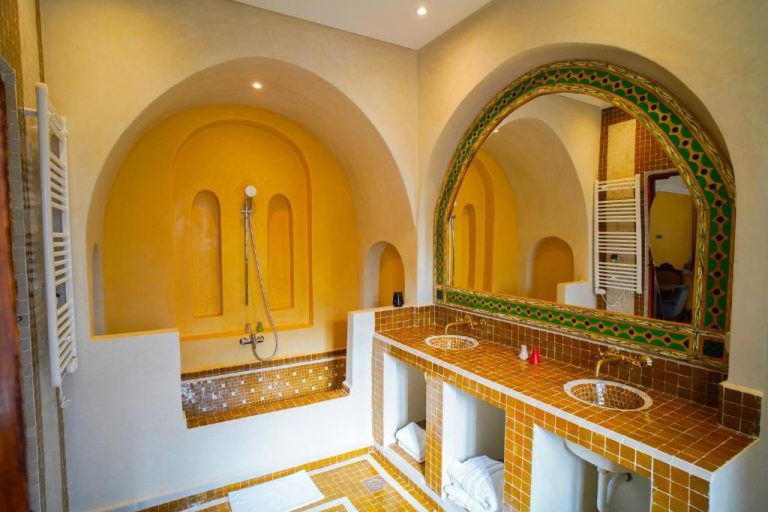 Baño de estilo marroquí con mosaicos dorados y espejo en arco del Kasbah Hnini