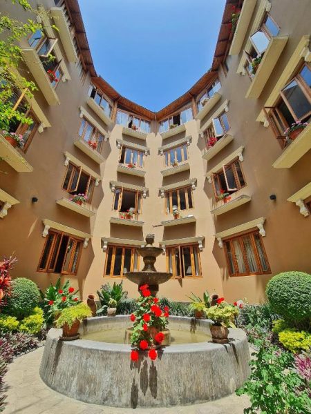 Patio interior con fuente ornamental y jardines del Hotel Antigua Miraflores rodeado de balcones floridos
