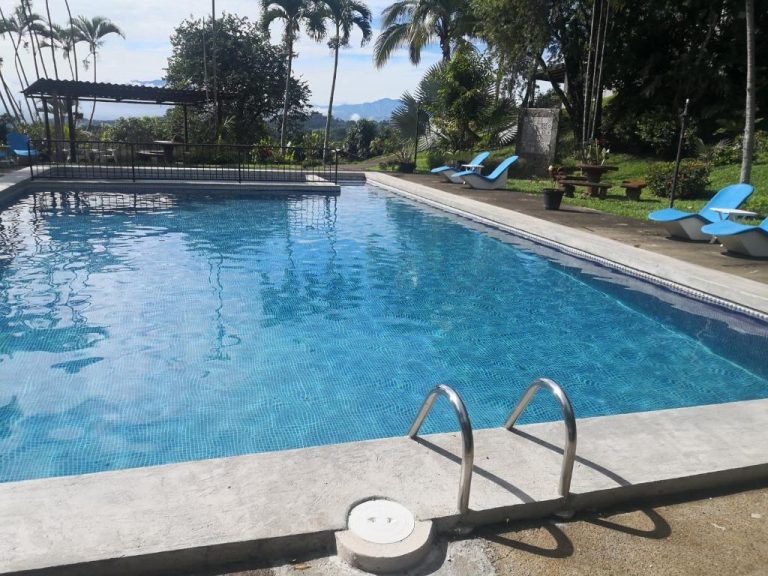 Piscina exterior con tumbonas azules y vista a las montañas en Hotel Villas de la Colina
