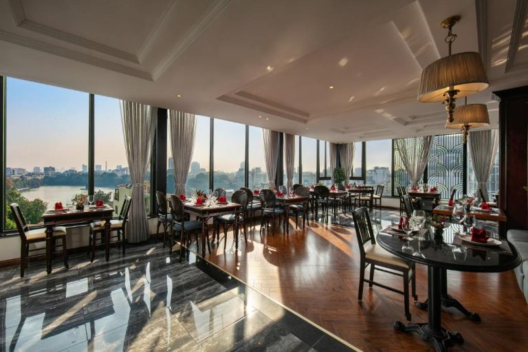 Restaurante rooftop con vistas panorámicas al lago del Lucien Hanoi Lakeside Hotel, mesas elegantes y grandes ventanales