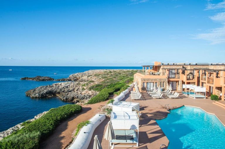 Piscina exterior con tumbonas y vistas al mar rocoso del Hotel Menorca Binibeca by Pierre & Vacances