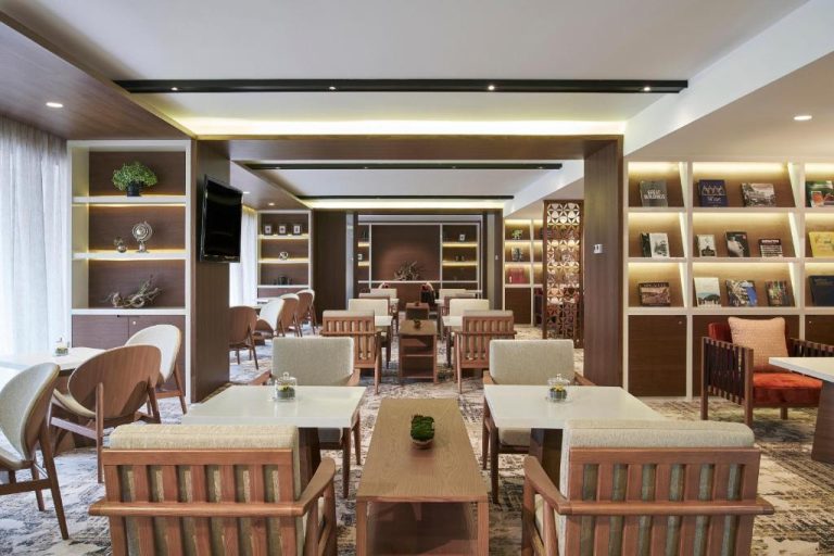 Zona lounge con mesas, sillas de madera y biblioteca iluminada en Orchard Rendezvous Hotel by Far East Hospitality
