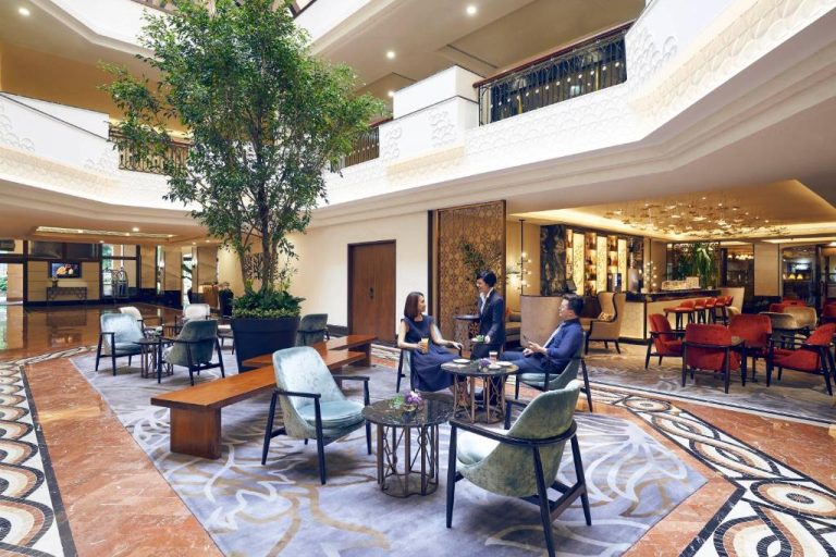 Elegante lobby lounge del Orchard Rendezvous Hotel con árboles interiores y clientes disfrutando de bebidas
