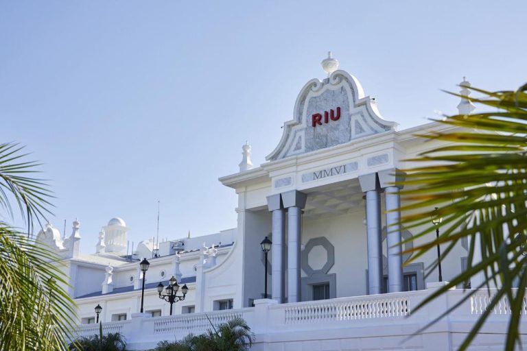 Fachada principal blanca del Riu Palace Riviera Maya con columnas clásicas y palmeras tropicales