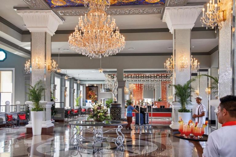 Lujoso lobby del Riu Palace Riviera Maya con grandes arañas de cristal y servicio de bienvenida con cócteles