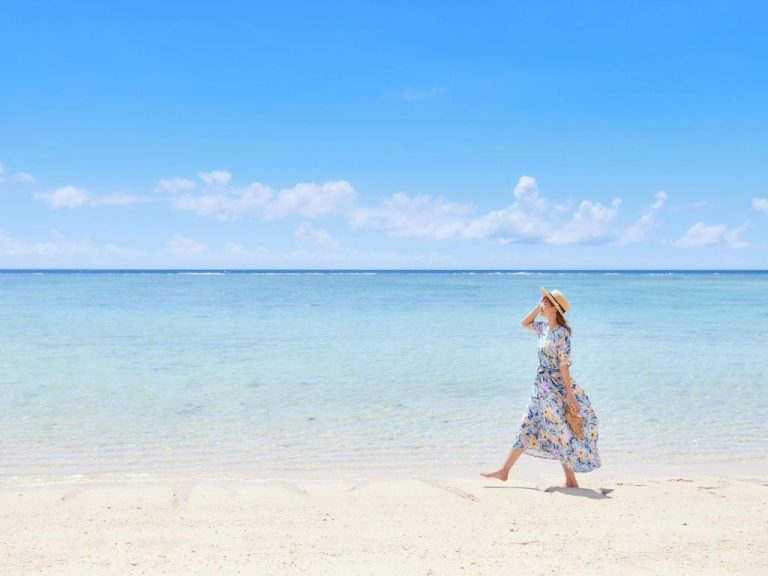 Mujer paseando por la playa de arena blanca y aguas turquesas del Hotel Nikko Alivila en Okinawa