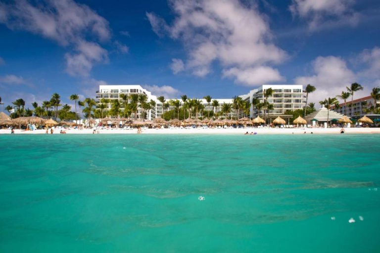 Vista desde el mar de la playa blanca del Aruba Marriott Resort & Stellaris Casino con sombrillas de palma