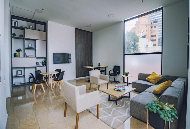 Sala de estar moderna con sofás, zona de trabajo y amplia ventana en el apartamento Enjoy In Bogotá