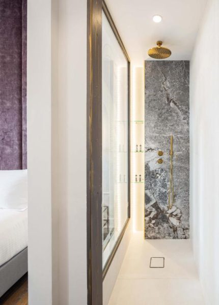 Ducha de lluvia con griferías doradas y pared de mármol gris en el Hotel Bella Venezia