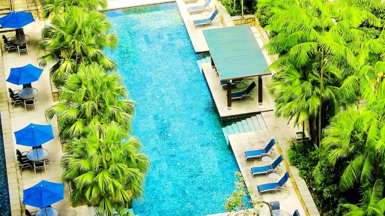 Piscina exterior del Amara Singapore rodeada de palmeras tropicales con tumbonas y gazebo