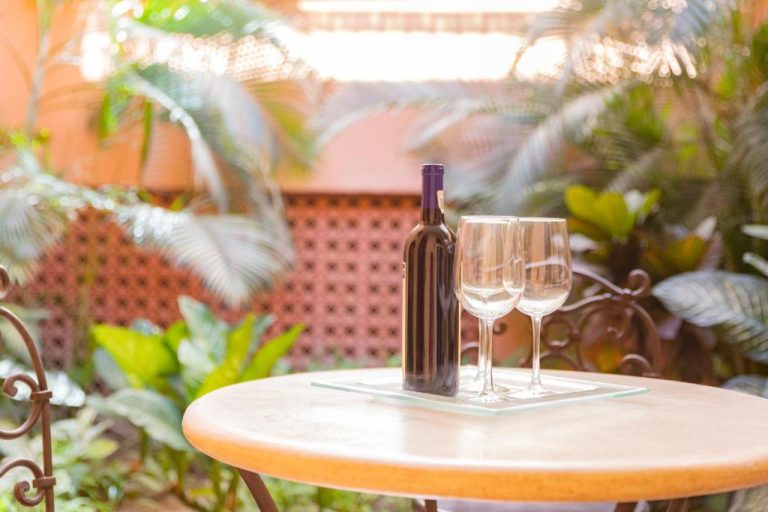 Botella de vino tinto con dos copas en terraza ajardinada del Hotel Colli