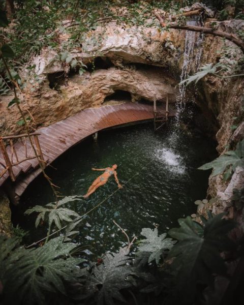 Cenote natural con cascada y pasarela de madera en Kan Tulum Hotel rodeado de vegetación tropical