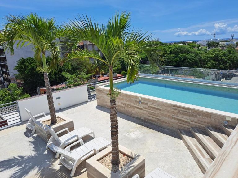 Terraza con piscina infinita y tumbonas rodeada de palmeras en Condo Kiaraluna Playa del Carmen