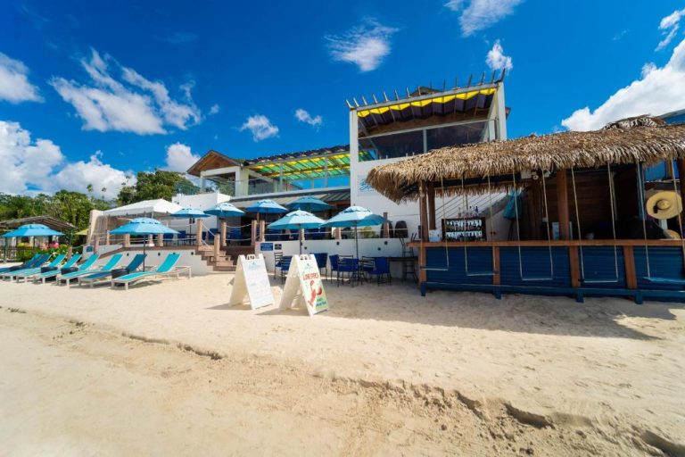 Bar tropical con techo de palapa y tumbonas azules en la playa de Blue Skies Beach Resort