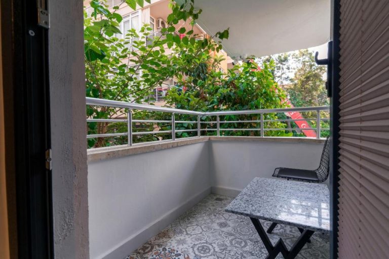 Balcón con mesa de mármol y silla metálica en Pasham Residence, rodeado de vegetación